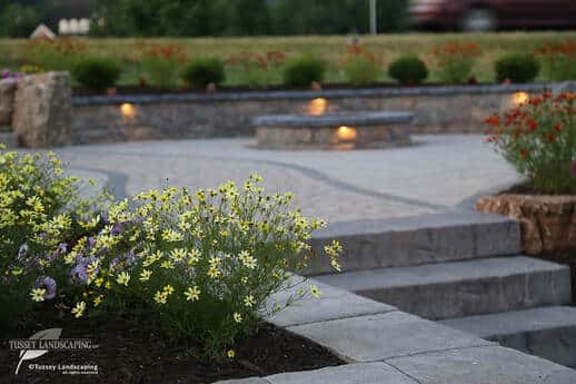 A stone walkway with flowers and a fire pit.