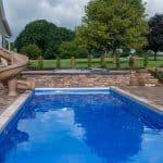 fiberglass swimming pool with slide and paver patio