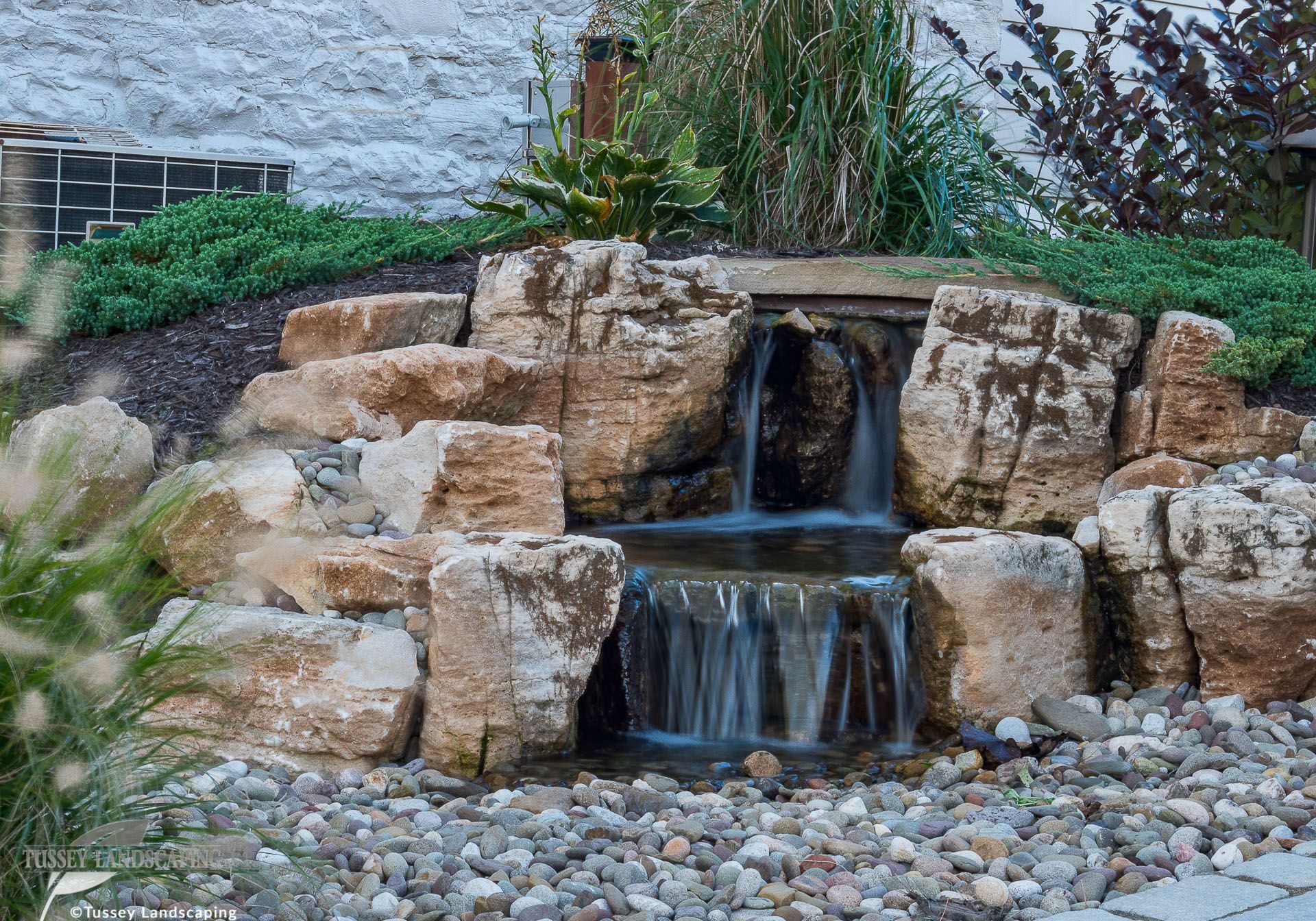 A small waterfall in a backyard with rocks and plants.